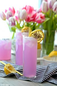 Lavender lemonade shown as pick in tall long glassesd. with flower in background and towel under glasses
