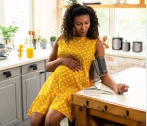 Woman in Yellow and while spot dress taking her Blood Pressure with the kitchen in background