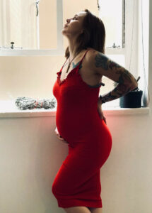 Pregnant woman in red dress suffering Pregnancy Back Pain with bathroom image in background.