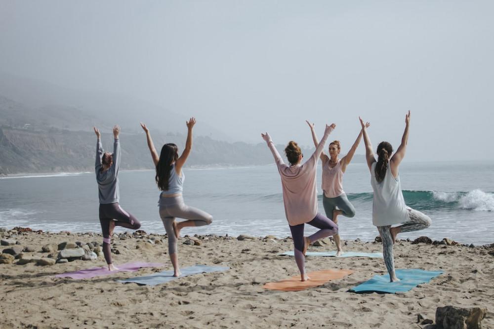 Group of People at the Beach enjoying Yoga with improving their Well-Being and taking Self-Care of themselves