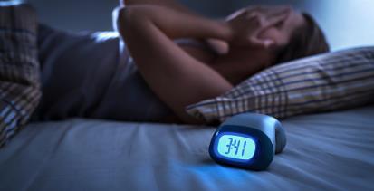 Woman laying in bed unable to sleep due to blue light issues clock on bed showing 3.41 AM