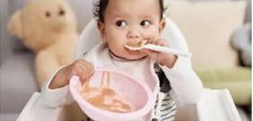 Baby eating solid soft food with teddy in background.